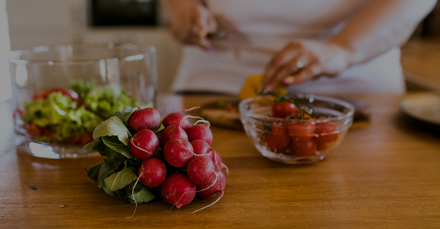 Radishes and a bowl strawberries sit on a counter while a woman prepares a healthy meal